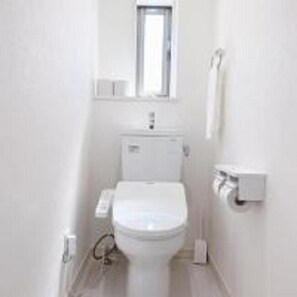 A small, white bathroom with a toilet, a window above the sink, and a towel dispenser on the wall. - OUCHI HOTEL Miyajimaguchi (Hatsukaichi)
