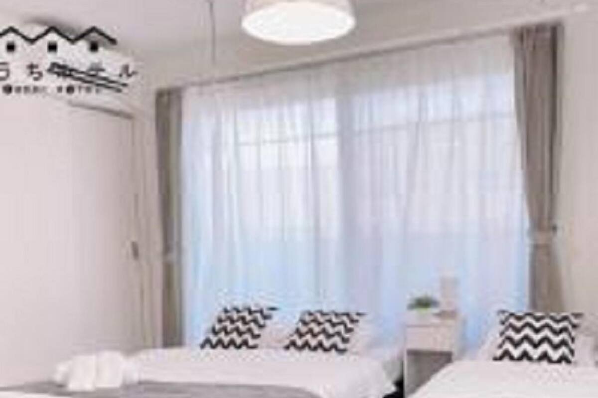 Une chambre d’hôtel moderne avec deux lits, une grande fenêtre avec des rideaux légers et un décor minimaliste.