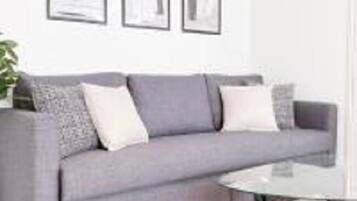 Una sala de estar moderna con un sofá gris, una mesa de centro de vidrio y obras de arte enmarcadas en la pared.