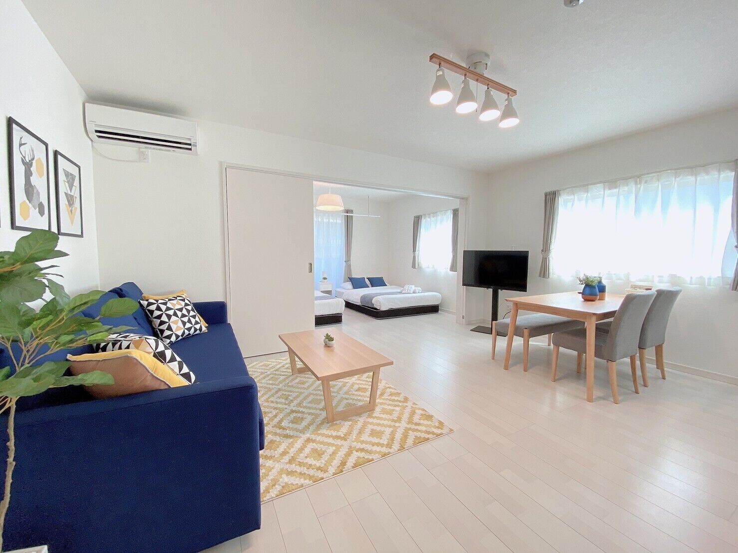 Una sala de estar moderna con un sofá azul, una mesa de centro y un televisor. Hay un comedor con una mesa y sillas.