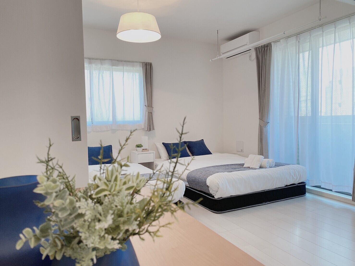 A modern bedroom with a bed, bedside tables, a hanging light fixture, and a large window with curtains.
