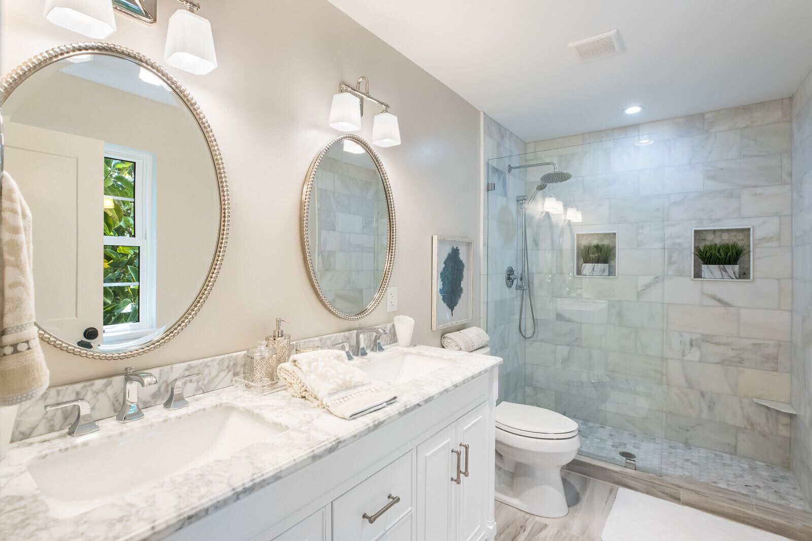 Une salle de bain dotée de deux grands miroirs, d’un comptoir en marbre, d’une douche à parois de verre et de toilettes.
