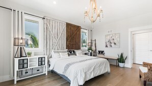 A bedroom with a large bed, a console table, a bench, a chandelier, and a door. - Funky Beach Farmhouse: Beautiful Bay views, heated pool, hot tub, lounge area (Anna Maria)