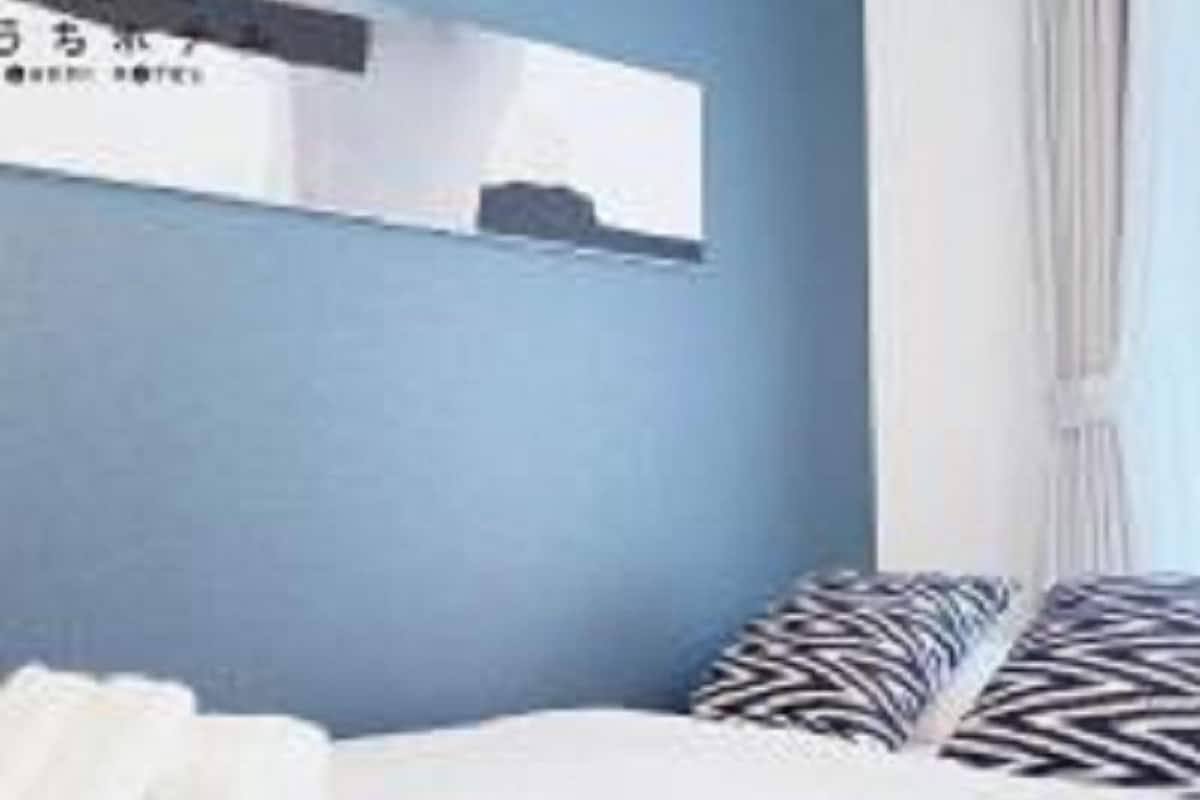 Ein Hotelzimmer mit Bett, Kissen, einem an der Wand befestigten Spiegel und einem Fenster mit Vorhängen.