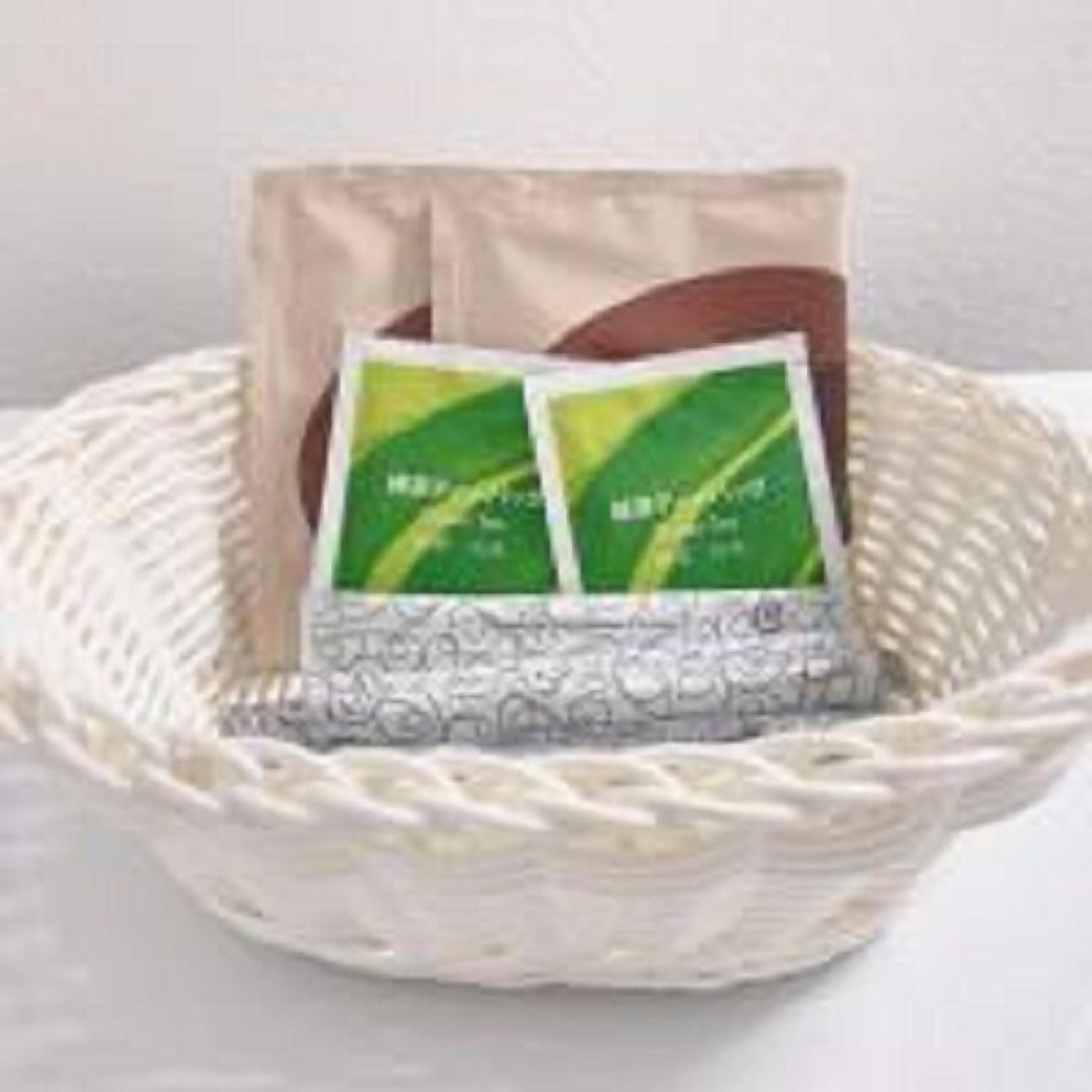 Una cesta tejida que contiene dos paquetes verdes, posiblemente té o productos herbales, sobre un fondo neutro.