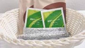 Una cesta tejida que contiene dos paquetes verdes, posiblemente té o productos herbales, sobre un fondo neutro.