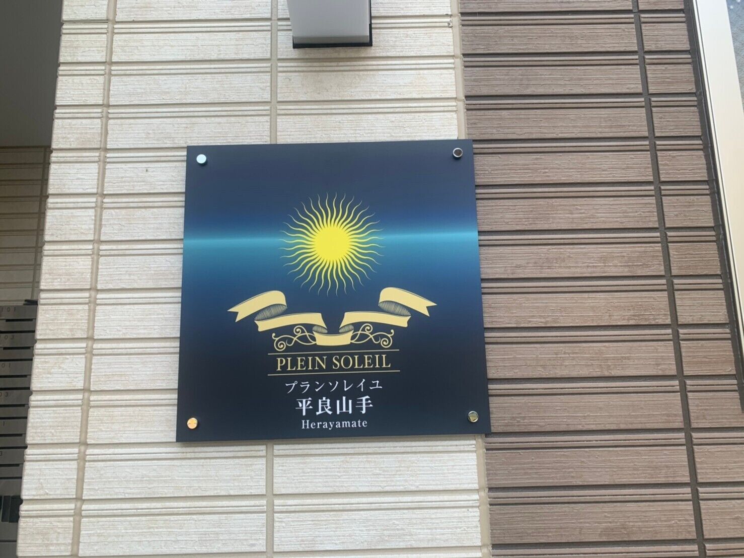 Ein Schild mit Sonnendesign und Schleife, mit Text auf Englisch und Japanisch.