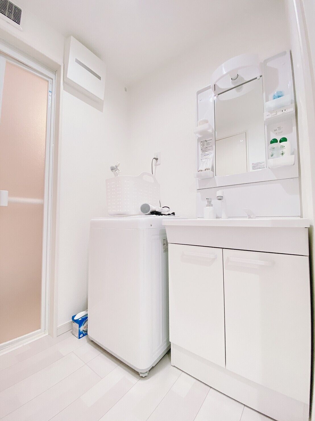 A compact, modern bathroom with a white sink, mirror, and a small laundry area.