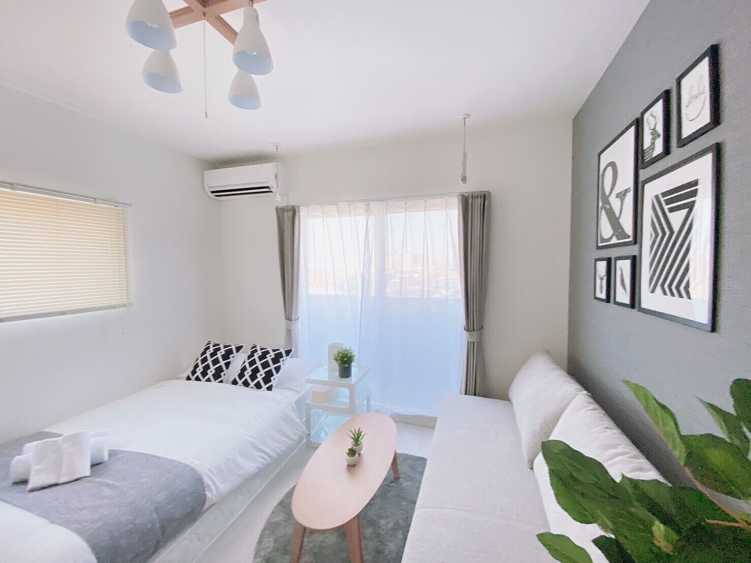 Un dormitorio moderno y luminoso con cama, una mesita con una planta, un sofá y una ventana con cortinas.