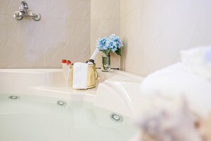 Un baño con bañera, un neceser dorado, un vaso de agua y un jarrón con flores azules.