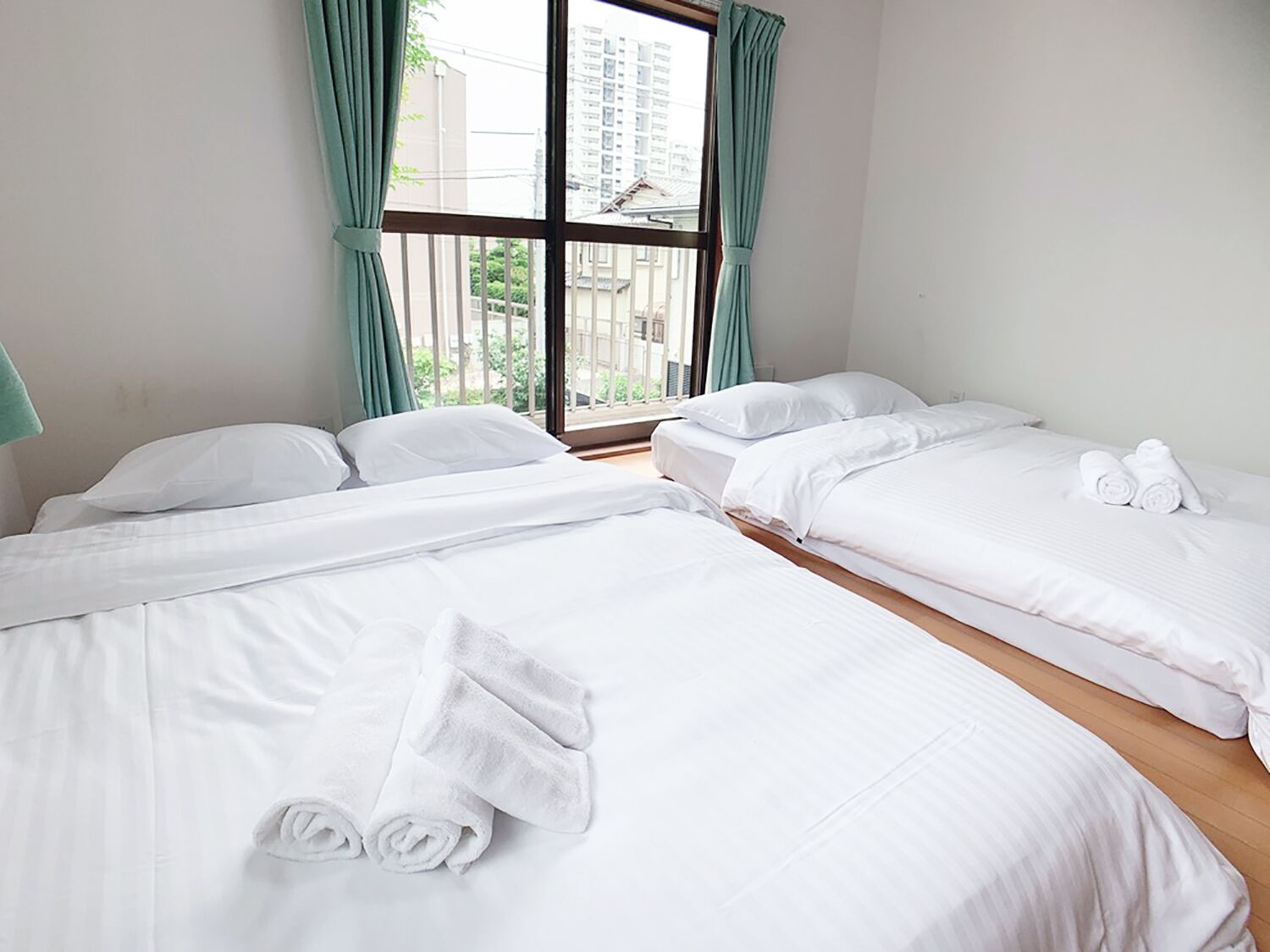 Ein Hotelzimmer mit zwei Betten, einem großen Fenster mit Vorhängen und Blick auf Gebäude.
