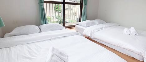 Ein Hotelzimmer mit zwei Betten, einem großen Fenster mit Vorhängen und Blick auf Gebäude.