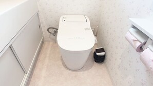 A small bathroom with a toilet, a toilet paper holder, and a trash bin. - Itsukaichi First Villa Hiroshima (Hiroshima)