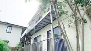 A two-story residential building with a balcony, a tree in front, and a neighboring house. - Itsukaichi First Villa Hiroshima (Hiroshima)
