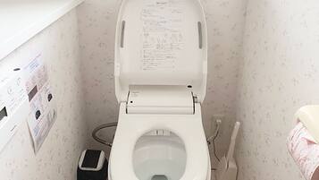 A small bathroom with a toilet, a hand dryer, and a paper dispenser.