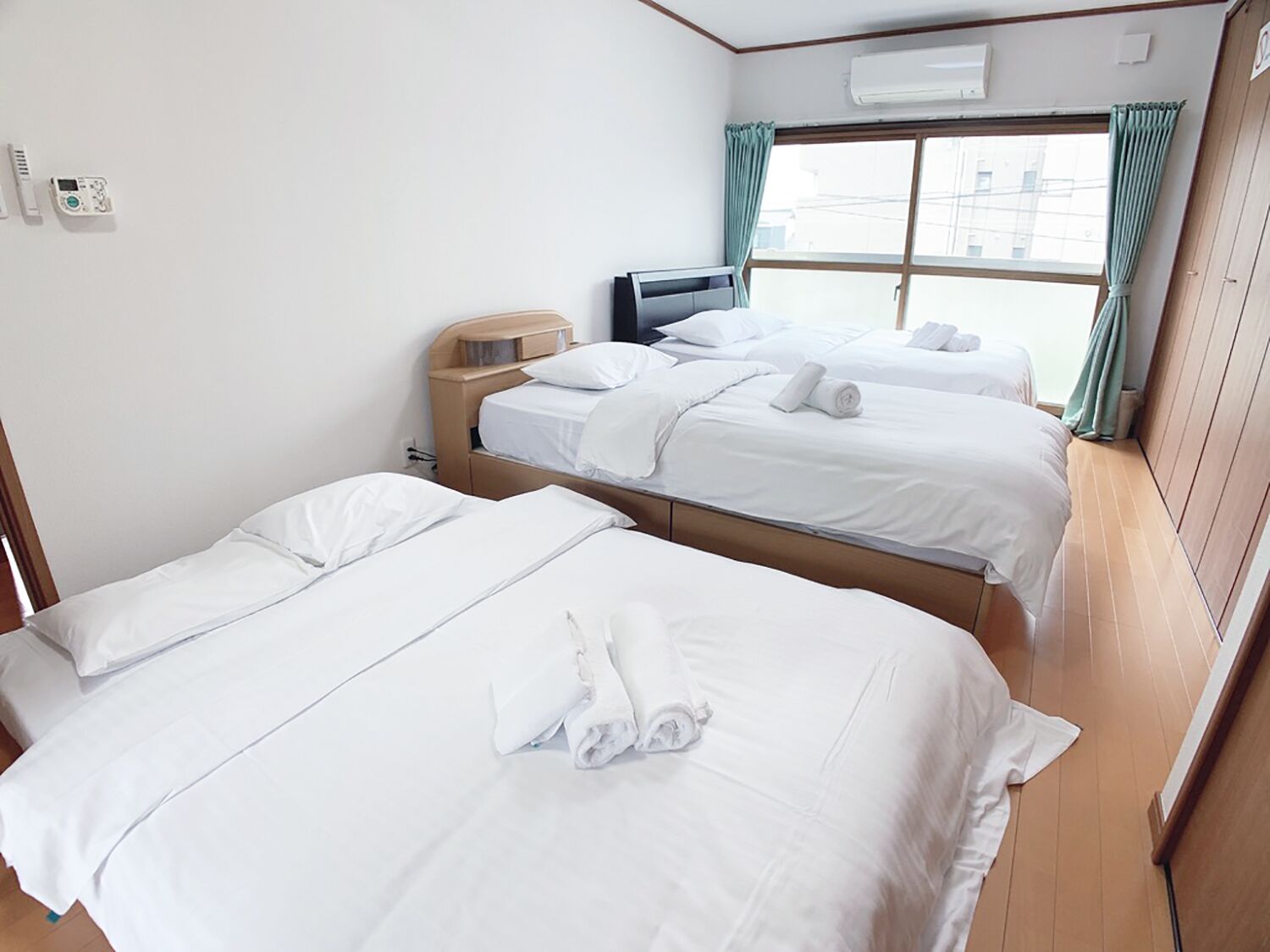 A hotel room with two single beds, a wooden headboard, a small desk, and a window with curtains.