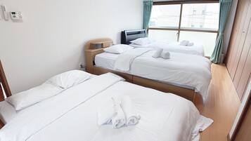 A hotel room with two single beds, a wooden headboard, a small desk, and a window with curtains.