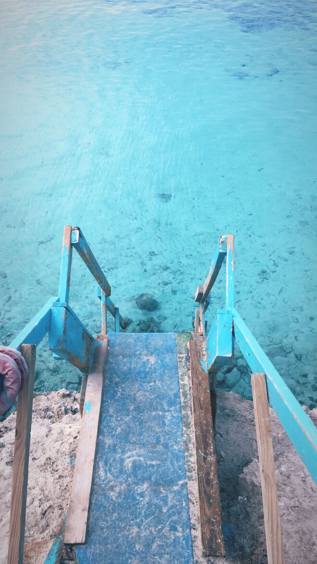 Un escalier en bois qui descend vers une eau d’un bleu cristallin.