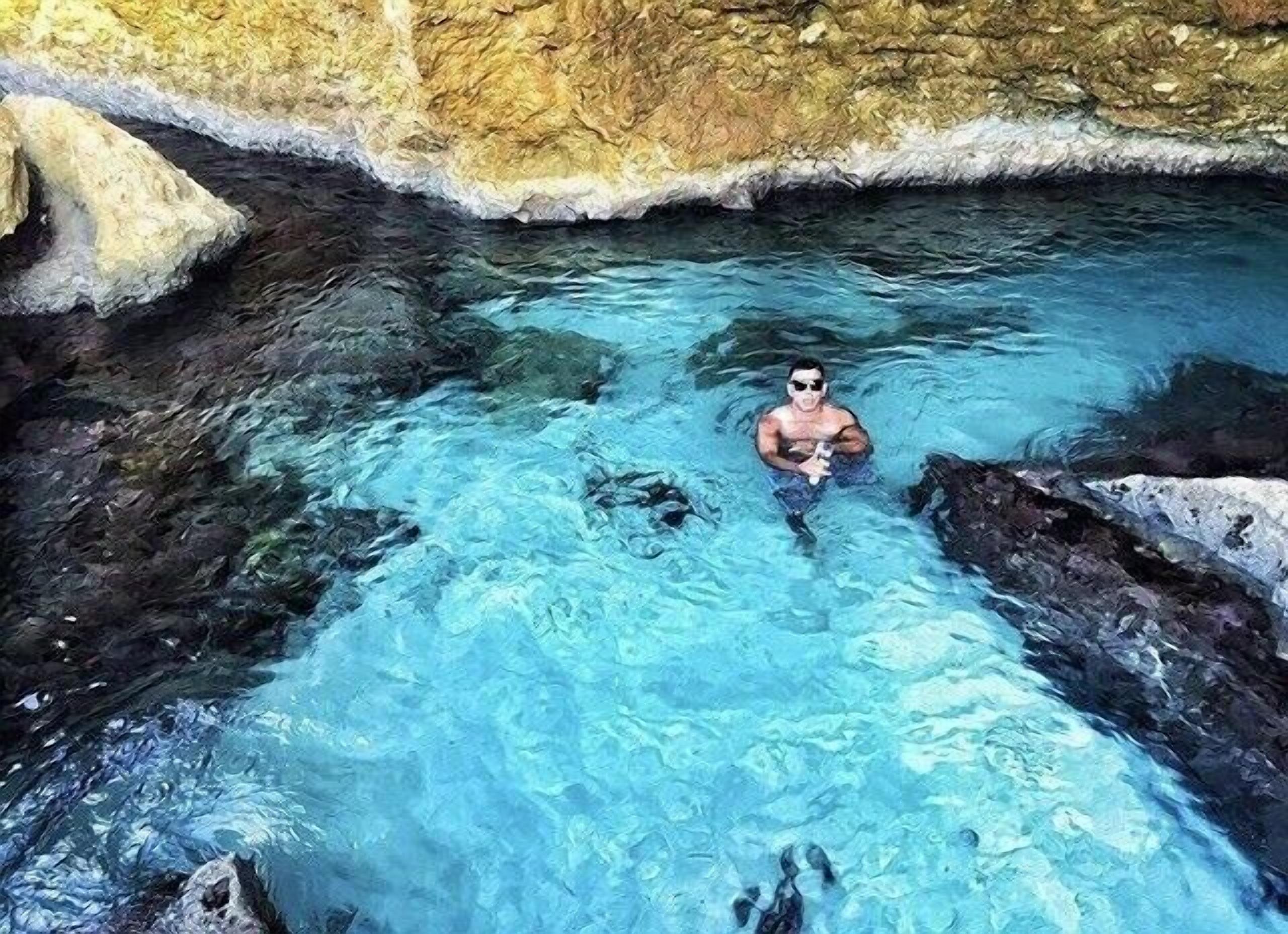 Uma pessoa nadando em uma piscina límpida, com pedras ao redor.