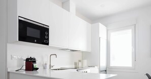 A modern kitchen with white cabinetry, a black microwave, and a stainless steel sink.