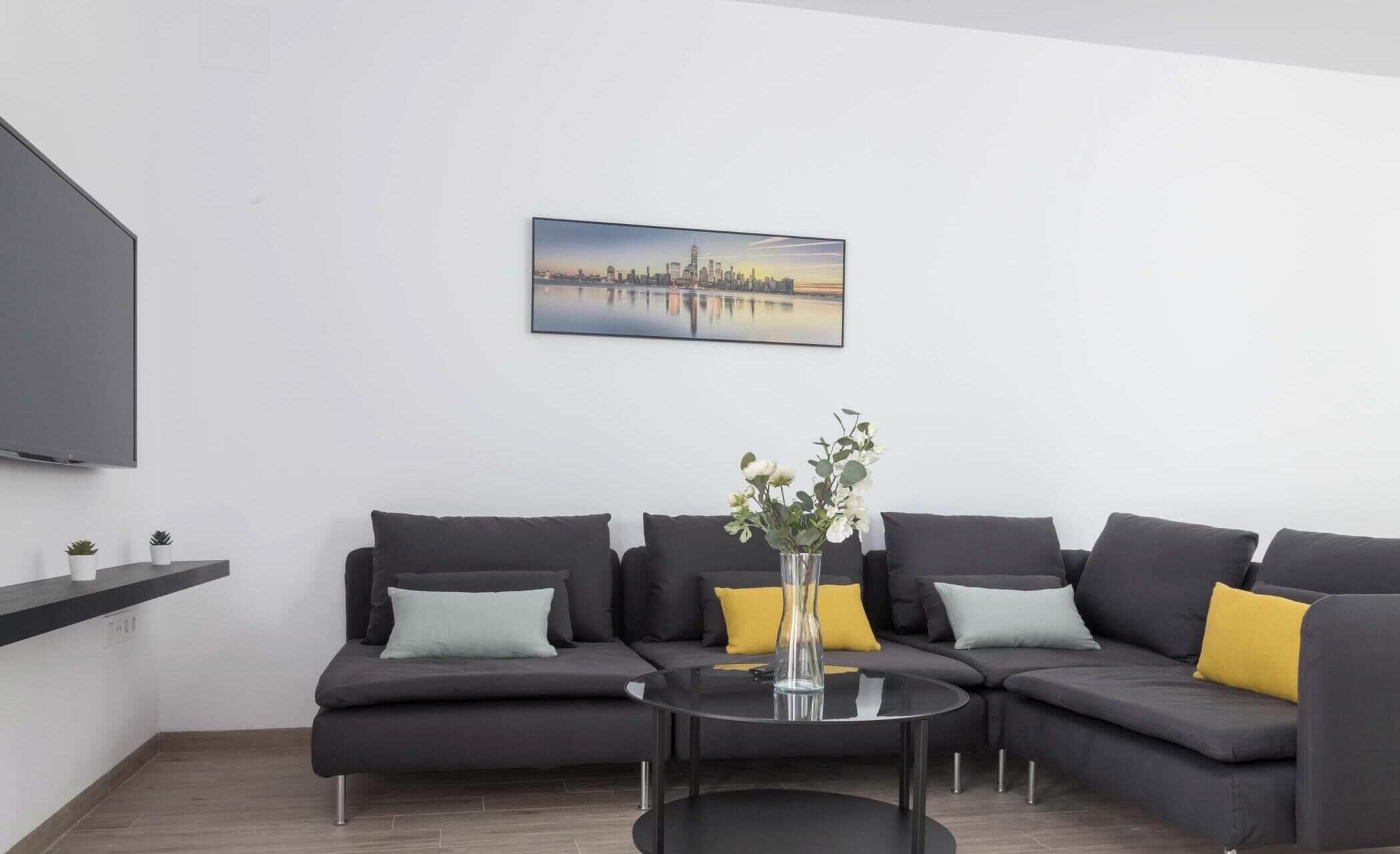 Una sala de estar moderna con un sofá modular, una mesa de centro de vidrio y una pintura de un paisaje urbano en la pared.