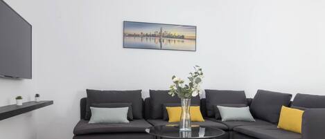 Una sala de estar moderna con un sofá modular, una mesa de centro de vidrio y una pintura de un paisaje urbano en la pared.