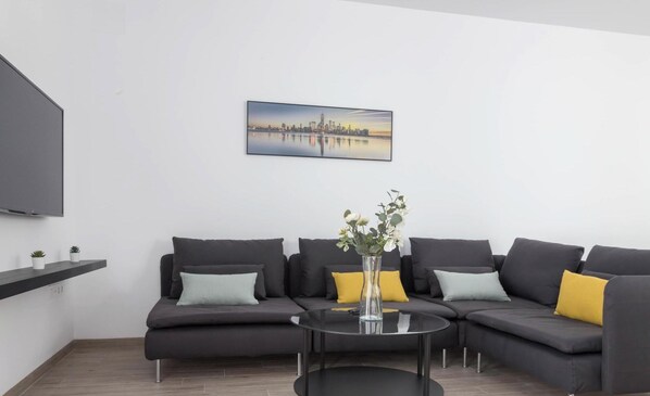 A modern living room with a sectional sofa, a glass coffee table, a flat-screen TV, and a cityscape painting on the wall. - Casa del Fotografo by Cadiz Time (Cádiz)