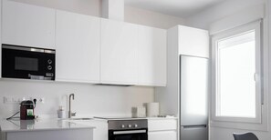 A modern kitchen with white cabinetry, a built-in microwave, a stove, and a refrigerator. - Casa del Fotografo by Cadiz Time (Cádiz)
