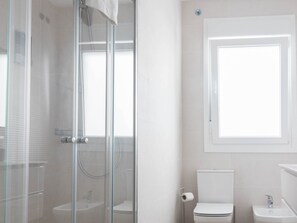 A bathroom with a glass-enclosed shower, a toilet, and a sink.