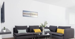 A modern living room with a grey sofa, a small round table, and a cityscape painting on the wall.