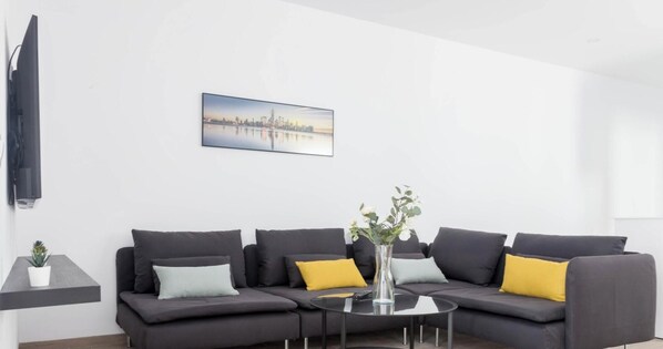 A modern living room with a grey sofa, a small round table, and a cityscape painting on the wall.