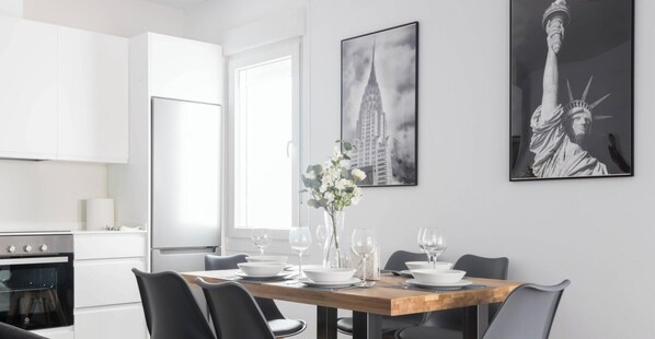 A modern kitchen with white cabinets, a wooden dining table set with white plates and glasses, and two framed pictures on the wall.
