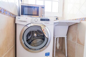 A compact washing machine with a digital display, a microwave above it, and a small sink with a tiled countertop.