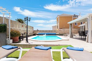 A swimming pool with lounge chairs, a pergola, and a stone wall.