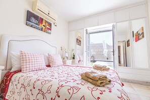 A hotel room with a bed, a nightstand, a mirror, and a view of the outside.