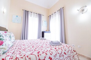Une chambre à coucher avec un lit, des rideaux, une table de chevet et un luminaire fixé au mur.