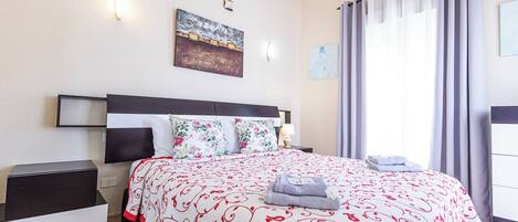 A neatly made bed with a patterned bedspread, a bedside table with a lamp, and a wall-mounted air conditioning unit.