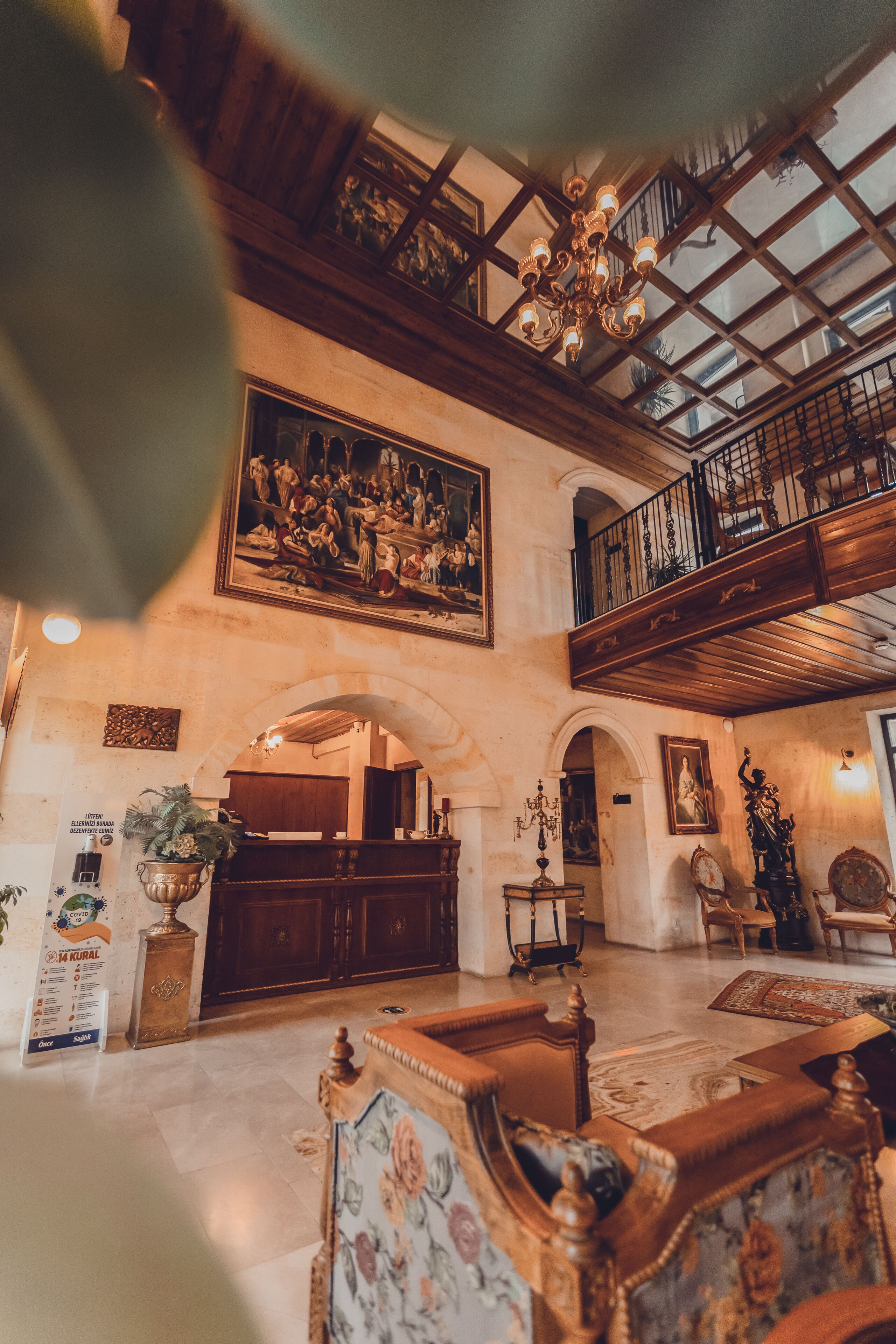 A spacious lobby with a high ceiling, a chandelier, a large painting, and a staircase leading to an upper level.