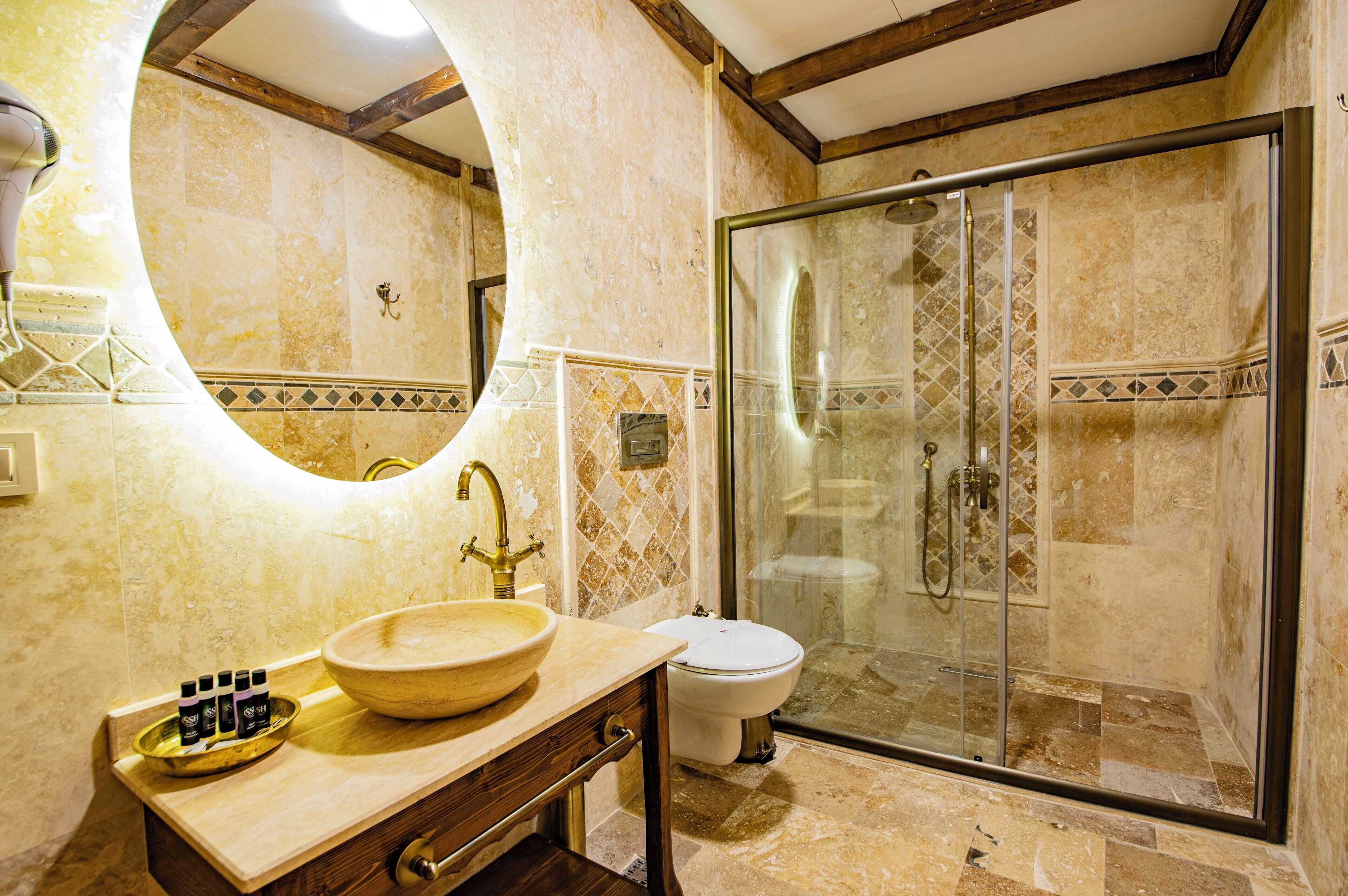 A bathroom with a large oval mirror, a wooden vanity, a bowl sink, and a glass-enclosed shower.