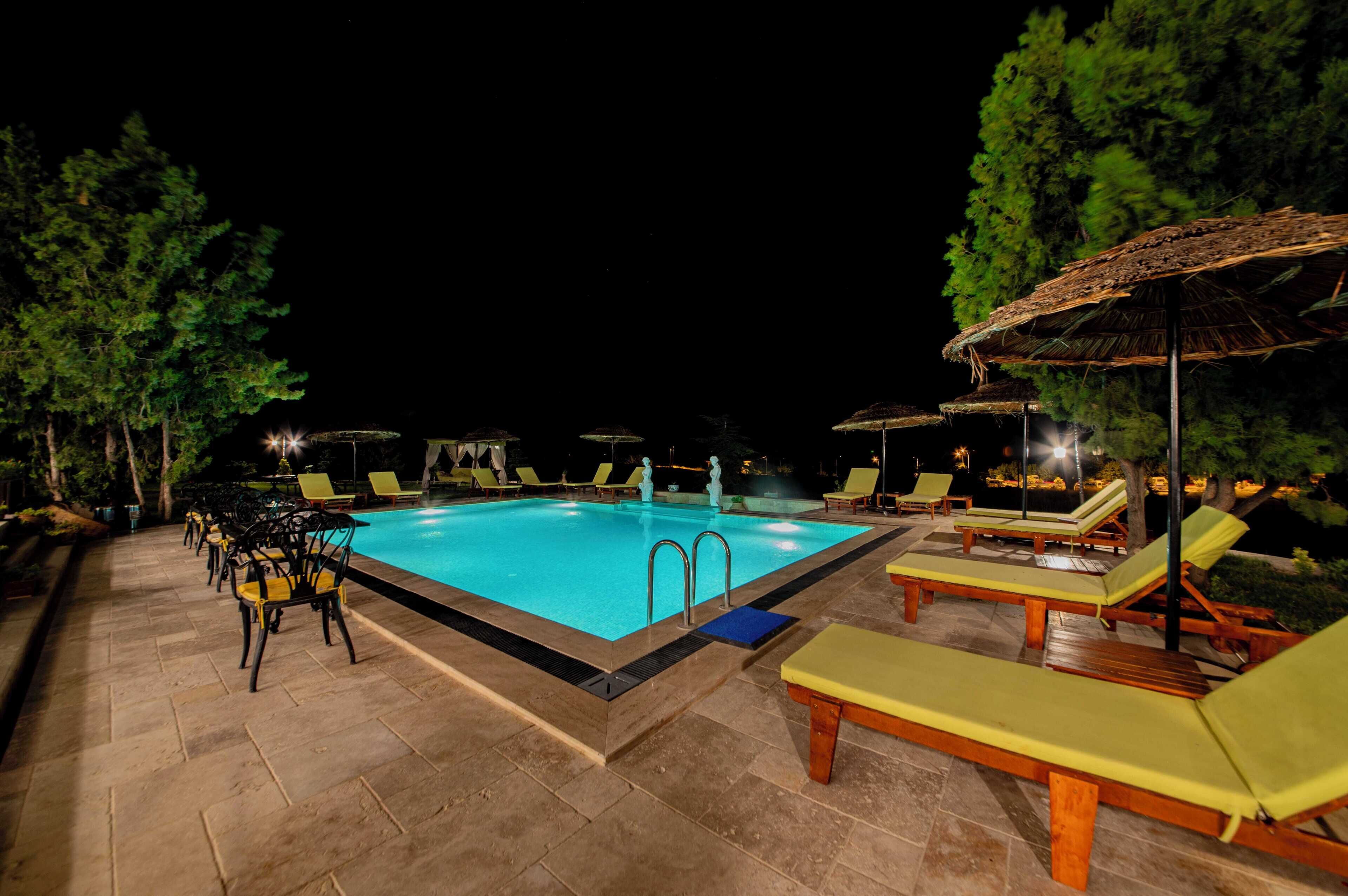 Piscina con sillones reclinables y sombrillas, rodeada de árboles.