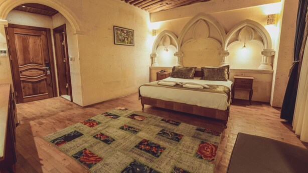 A bedroom with a wooden floor, a bed with a patterned bedspread, a nightstand, and a wall-mounted light fixture. - Sobek Stone House Cappadocia (Nevsehir)