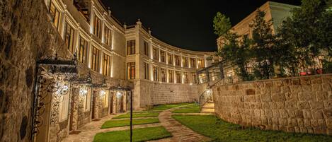 A stone building with a curved facade, a central courtyard with a stone pathway, and a staircase leading to an upper level.