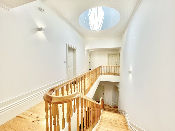 Un interior amplio con una escalera de madera, un tragaluz y una puerta que da a otra habitación.