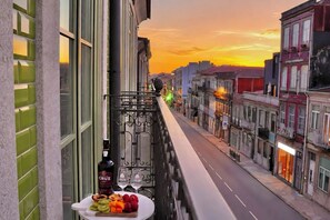 Ein Balkon mit Obstteller und Weinflasche, mit Blick auf eine Straße, Gebäude und einen Sonnenuntergang.