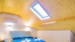 A bedroom with a sloped ceiling, a skylight, a bed with blue bedding, and an air conditioning unit. - Porto Domus 210 Penthouse (Porto)