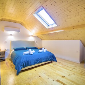 A bedroom with a sloped ceiling, a skylight, a bed with blue bedding, and an air conditioning unit. - Porto Domus 210 Penthouse (Porto)