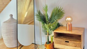 A room with a wooden floor, a round mirror, a tall floor lamp, a potted plant, and a wooden side table with a globe lamp.