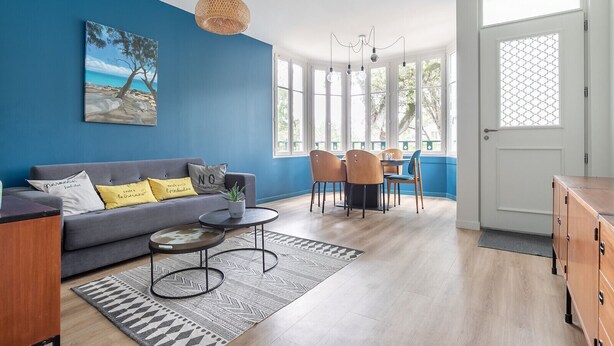 A modern living room with a blue accent wall, a sofa with cushions, a coffee table, and a dining area with chairs and a table. - House for 5 people - 500m from the beach (Noirmoutier-en-l´Ile)