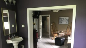 A bedroom with a bed, a bedside table, a mirror, a sink, and a chair.