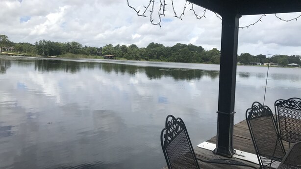 A covered outdoor seating area with metal chairs and a view of a calm lake.